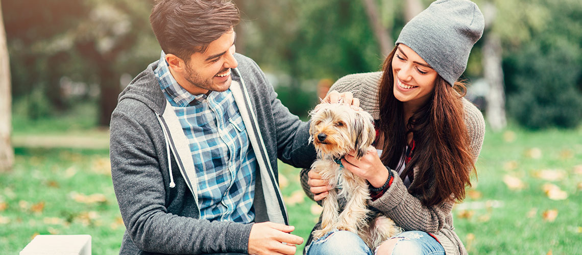a young man and young woman petting a dog at a park